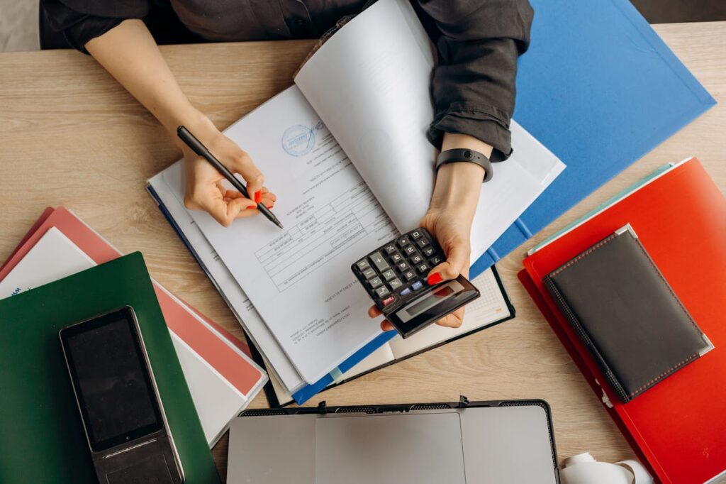 Personne effectuant des calculs sur des documents papier à un bureau, illustrant la gestion administrative professionnelle.